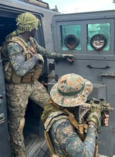 two men in camouflage gear are getting out of a vehicle and pointing at the door