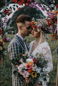 a man and woman are standing under an arch with flowers on the head, holding each other