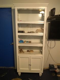 a white bookcase with glass doors and shelves on the bottom, in front of a blue door