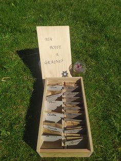 a wooden box filled with knives on top of a grass covered field next to a sign