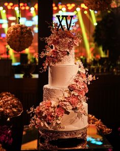 a three tiered cake with flowers on the top is sitting on a table in front of other desserts