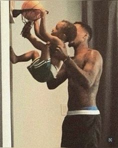 a man holding a basketball while standing next to a little boy on his lap with the ball in his hand