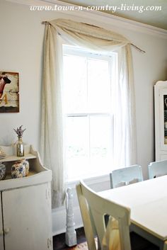 a white dining room table and chairs in front of a window with curtains on the windowsill