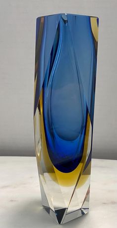 a blue glass vase sitting on top of a white table next to a gray wall