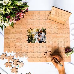 a person holding a piece of puzzle next to flowers and a wooden box with a photo on it