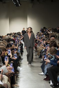 a model walks down the runway in front of a large group of people taking pictures