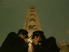 two men sitting next to each other in front of a tall building with writing on it