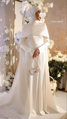 a woman in a white wedding dress and veil standing next to a flower arrangement with flowers