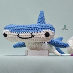 a crocheted blue and white stuffed shark toy with toothbrush in it's mouth