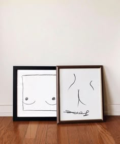 two framed drawings sitting on top of a wooden floor