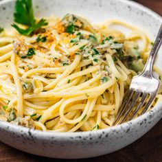 a white bowl filled with pasta and parsley on top of a wooden table next to a fork