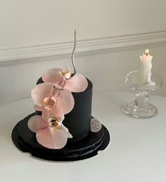 a black hat with pink orchids on top and two candles in the middle, sitting on a white table