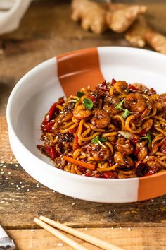 a white bowl filled with noodles and meat on top of a wooden table next to chopsticks