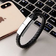 a black leather bracelet sitting on top of a laptop computer next to an apple phone