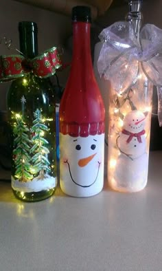 three wine bottles decorated with snowmen and christmas lights are sitting next to each other