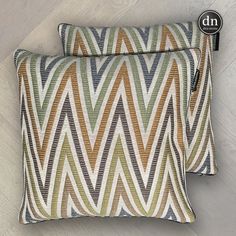 two decorative pillows sitting on top of a wooden floor next to each other, one with an orange and green zigzag pattern