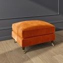 an orange ottoman sitting on top of a hard wood floor next to a gray wall