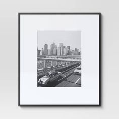 a black and white photo of a city with cars driving on the road in front of it