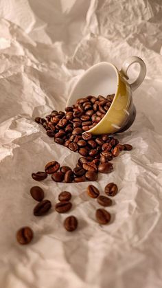 coffee beans spilling out of a white cup on top of crumpled paper with a half peeled banana