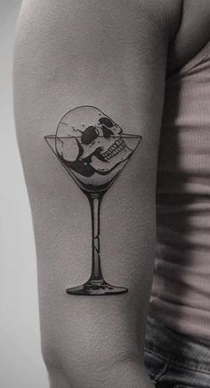 a man's arm with a skull in a martini glass tattoo on the left upper arm