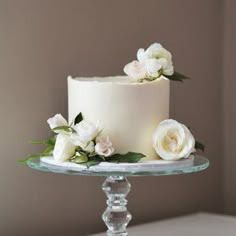 there is a white cake with flowers on the top and bottom tier, sitting on a glass stand