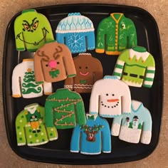 decorated cookies are arranged in the shape of sweaters and jumpers on a black tray