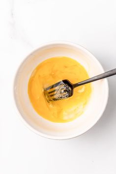 a white bowl filled with yellow liquid and a spoon