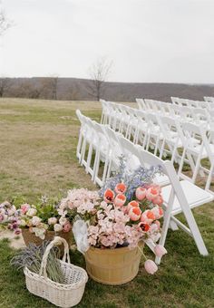 an outdoor ceremony setup with white chairs and flowers in a basket next to the aisle