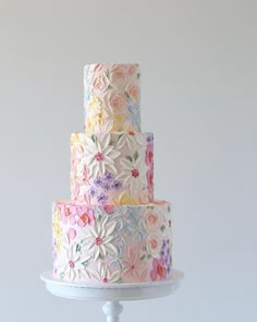 a multi - tiered cake decorated with flowers and leaves on a white stand against a gray background