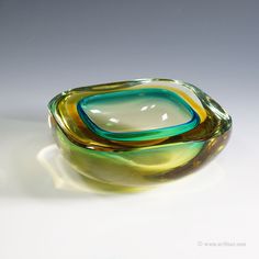 a green and yellow glass bowl sitting on top of a white tablecloth covered floor