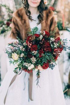 a woman in white dress holding a bouquet with red flowers and greenery on it