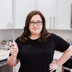 a woman holding a whisk in her right hand and looking at the camera