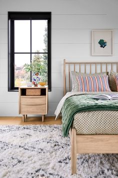 a bed room with a neatly made bed next to a window and a rug on the floor