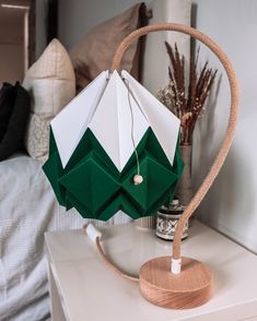 a green and white origami lamp sitting on top of a table next to a bed