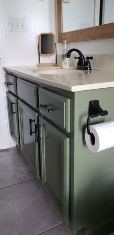 a bathroom with green cabinets and a white counter top next to a mirror on the wall