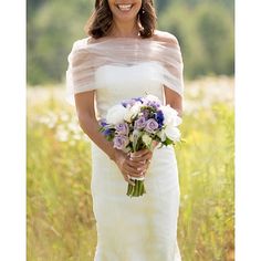 a woman in a white dress holding a bouquet of flowers and smiling at the camera