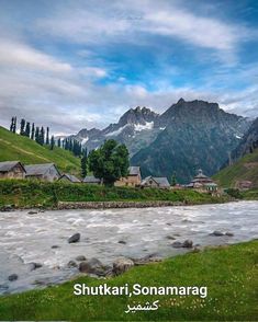 a river flowing through a lush green hillside covered in snow - capped mountains under a blue cloudy sky