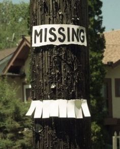 a telephone pole that has some stickers on it and is covered in paper with the word missing