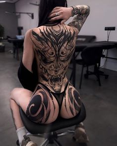 a woman with tattoos on her back sitting on a chair in an office space,