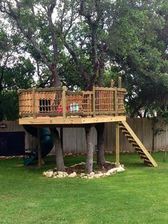 a tree house built into the side of a fenced in area with a slide