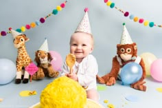 a baby is sitting in front of some stuffed animals and balloons with party hats on