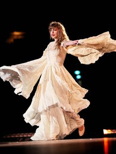 a woman in a white dress is dancing on stage with her arms spread out to the side