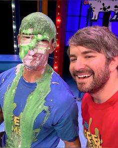 two men covered in green and white paint posing for the camera with one man's face painted