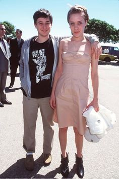 a man and woman standing next to each other in a parking lot with people behind them