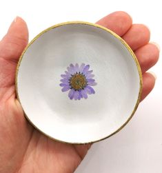 a hand holding a small white bowl with a purple flower on the inside of it