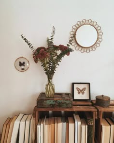 a vase filled with flowers sitting on top of a book shelf next to a mirror