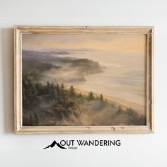 a painting hanging on the wall above a wooden frame with an image of trees and fog