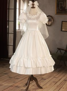 a white wedding dress on display in a room with wooden flooring and large windows