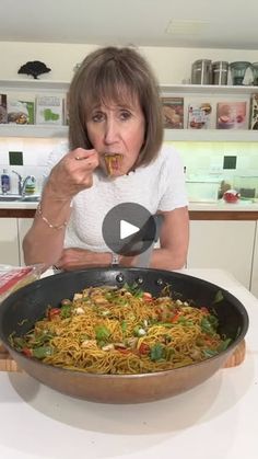 a woman eating spaghetti in a wok on the kitchen counter with her fingers up to her mouth