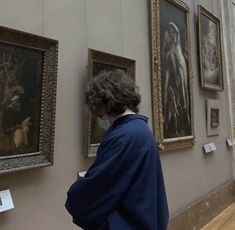 a woman looking at paintings on display in a museum